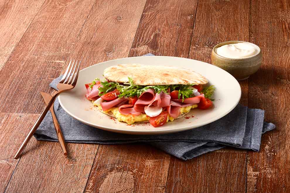 beirute de mortadela dentro de um prato branco de porcelana com talheres ao lado e em cima de um pano azul escuro, em cima de uma mesa