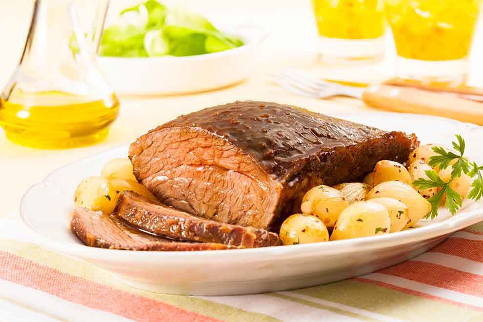 maminha assada com mini cebolas caramelizadas dentro de um prato branco de porcelana em cima de um jogo americano em pano de cor clara e listras