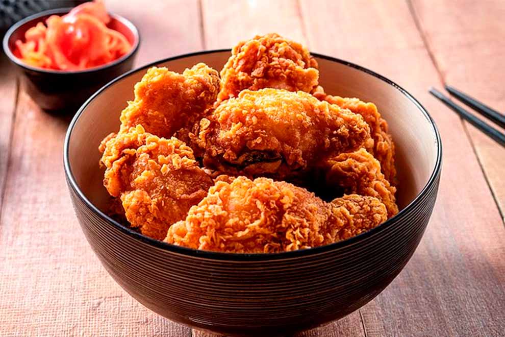 frango frito japones dentro de um pequeno bowl preto com hashi ao lado em cima de uma mesa 