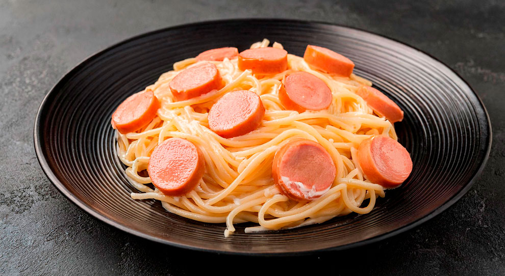 Prato de macarrão com salsichas em um fundo escuro