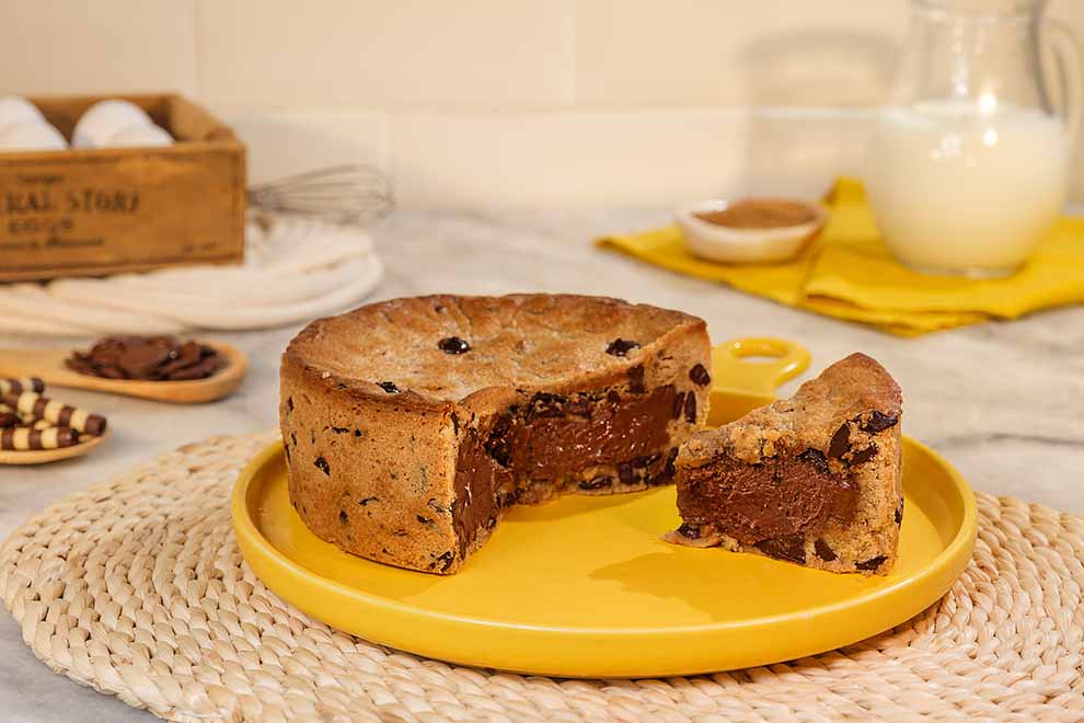 torta de cookie com gotas de chocolate, recheado com chocolate em cima de um pequeno prato amarelo e em cima de um jogo americano de palha