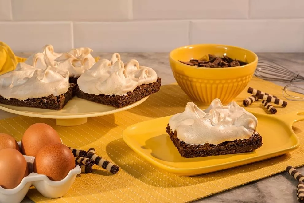 Brownie com suspiro em um prato amarelo com ovos em volta