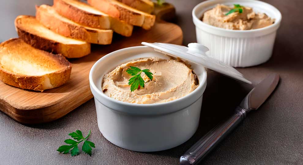 Uma tabua de corte com pedaços de pão tostado em cima e ao lado dois potes com patê de frango