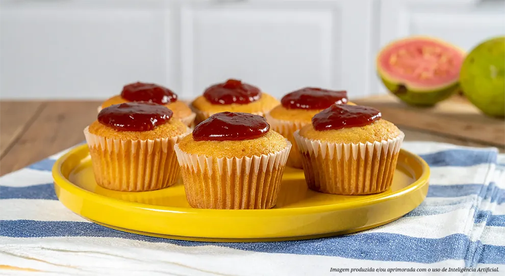 Composição de "Cupcake de fubá com goiabada na airfryer". Seis bolinhos de fubá, assados em forminhas, são decorados com goiabada. As goiabas frescas, inteiras e cortadas ao meio, aparecem desfocadas.