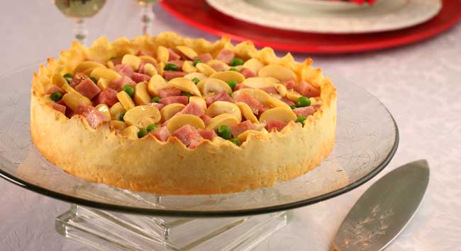 Torta de ricota e tender, feita com cogumelos e tomates assados, servida em um prato de vidro para torta.