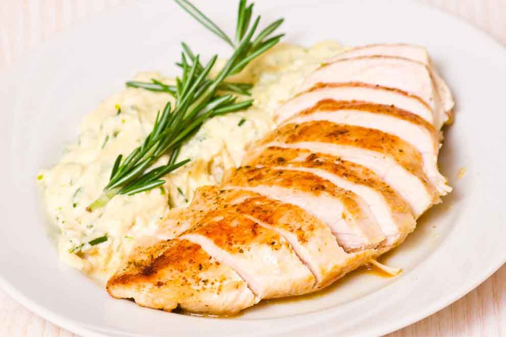 filé de frango fatiado com creme de milho ao lado dentro de um prato branco de porcelana e em cima de uma mesa branca