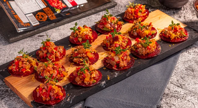 Chips de salame crocantes servidos com antepasto colorido de berinjela em tábua rústica.
