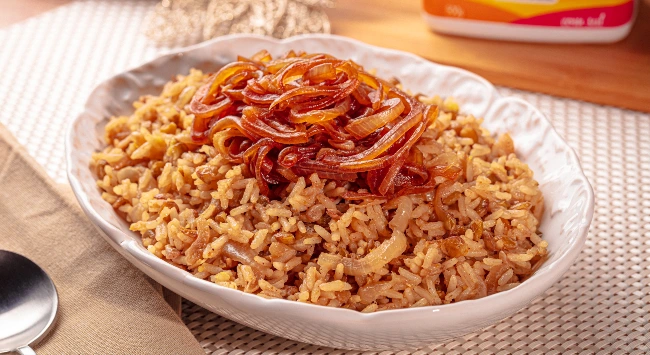 Arroz com lentilha coberto por cebola caramelizada dourada, servido em uma travessa branca.