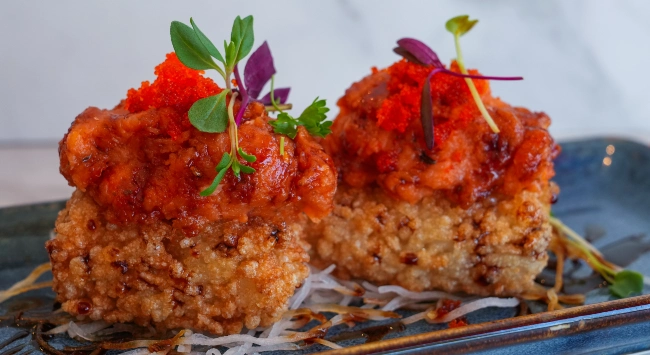 Cubos de arroz crocante cobertos com tartar de peixe apimentado, ovas e microverdes, servidos sobre fios de nabo em prato sofisticado.