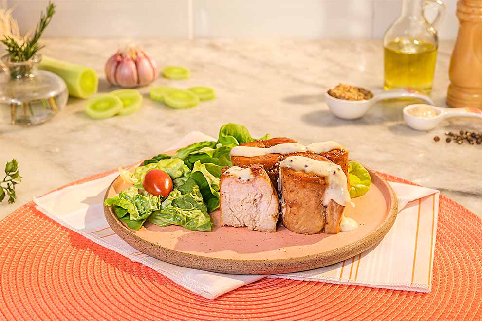 medalhão de frango feito na airfryer com salada dentro de um prato de porcelana rosado, em cima de um pano branco com listras coloridas e em cima de um jogo americano redondo alaranjado