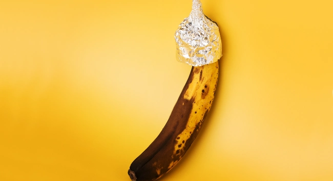 Ponta de uma banana enrolada com papel alumínio e fundo no tom amarelo bem vivo.