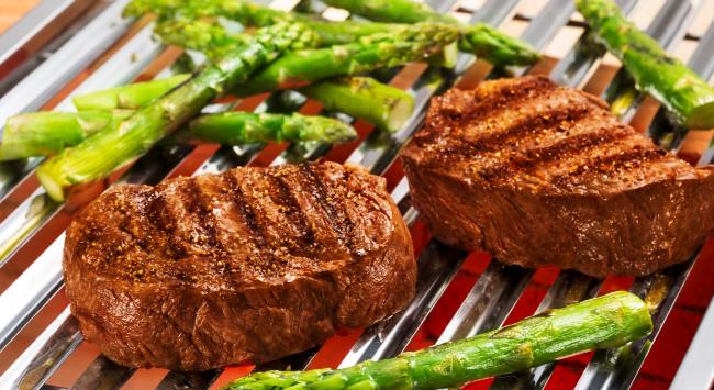 Dois bifes de ancho bovino grelhados na churrasqueira e servidos com aspargos. 