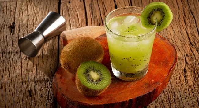 caipirinha de kiwi ao lado de kiwi picado e dosador de cachaça