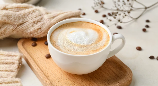 Cappuccino em uma xícara branca em cima de uma tábua de madeira.