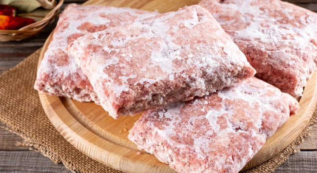 Uma tábua de madeira simples servindo como base para diversas porções de carnes congeladas. 