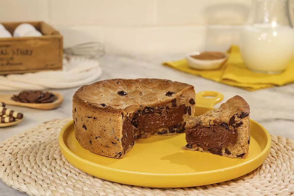 Torta de cookie recheada em cima de um suporte para tortas amarelo, sob uma mesa de mármore.