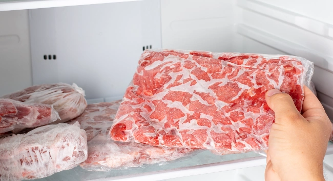 Pessoa tirando uma porção de carne congelada no congelador. 