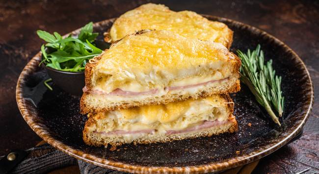 Croque Monsieur recheado com queijo e presunto servido em prato redondo escuro