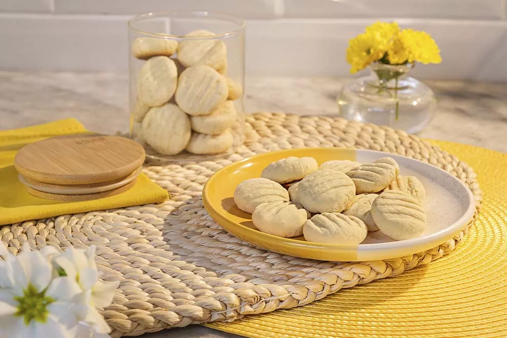 Imagem de diversos Biscoitos de nata em cima de um prato amarelo e branco, sob uma mesa de mármore, com alguns biscoito em um pote de vidro ao fundo  