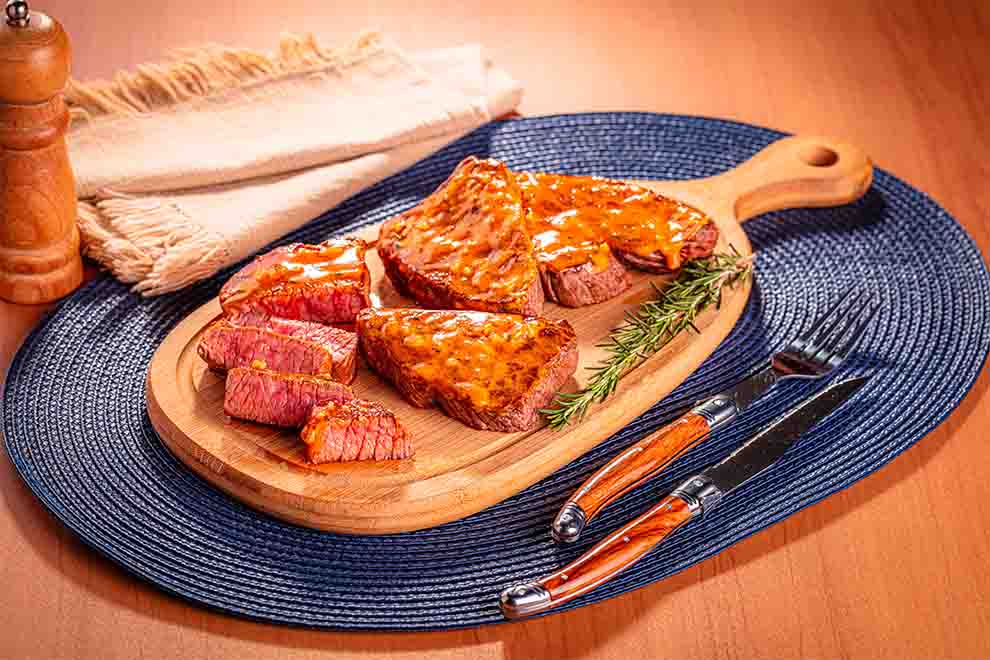 churrasco maminha na airfryer com um ramo de alecrim ao lado em cima de uma tábua de madeira e talheres ao lado em cima de um jogo americano azul redondo