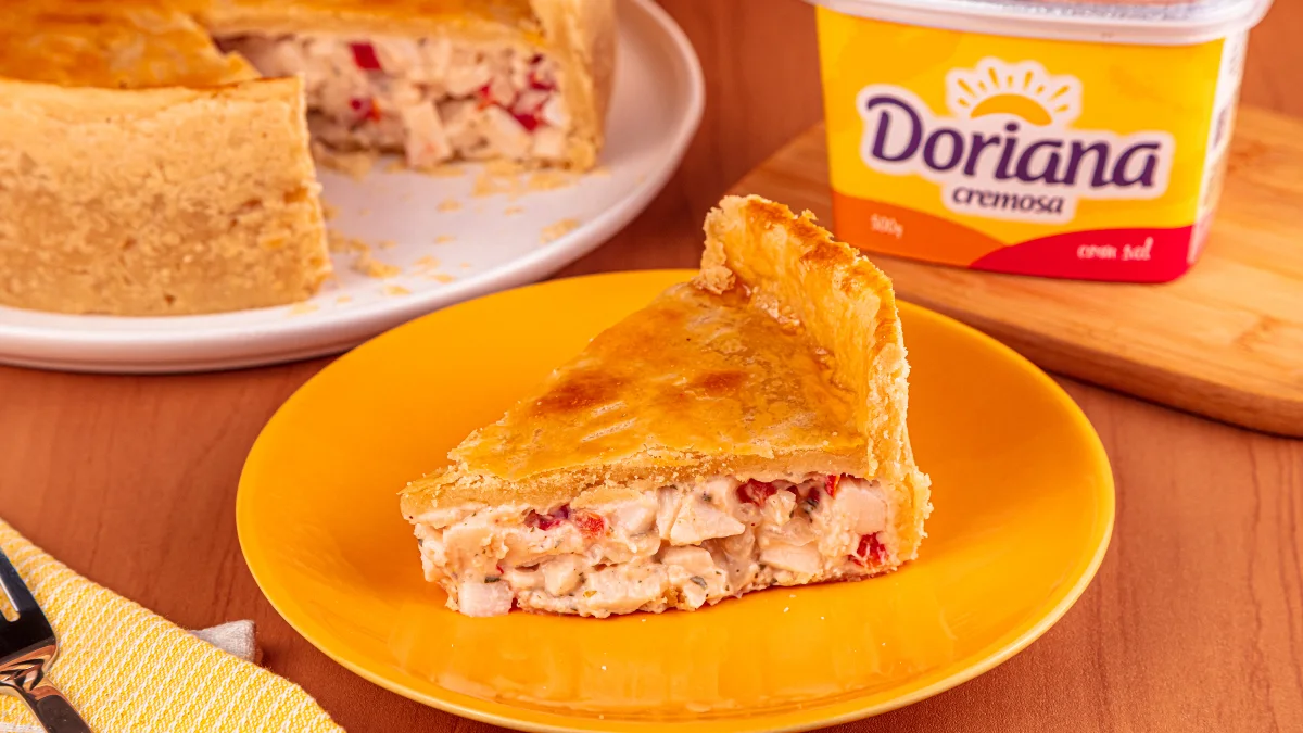 Empadão de palmito com muito recheio servido em um prato amarelo e com Doriana ao fundo.