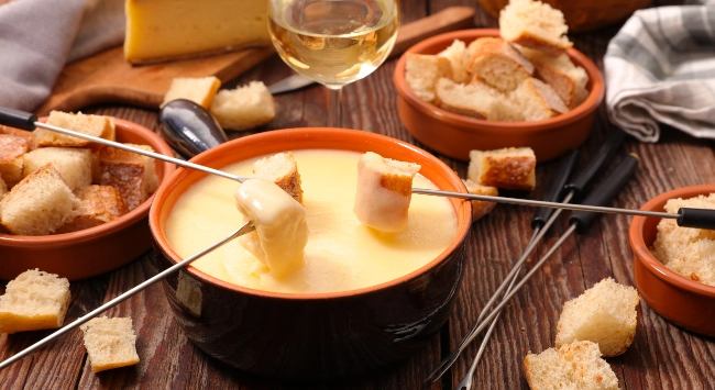 Porção de fondue de queijo acompanhado de pão cortado.