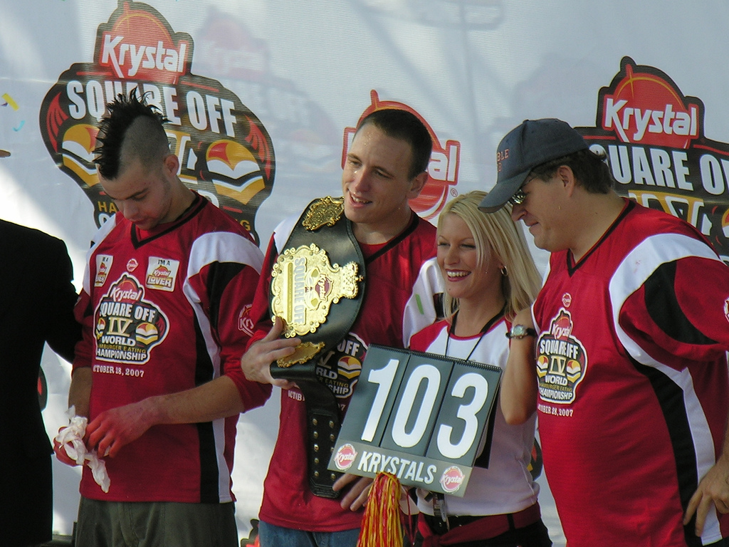 Homem ostentando título de quem come mais hambúrgueres por minuto.