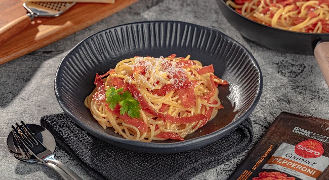 Macarrão carbonara com pepperoni servido em um prato fundo preto com listras.