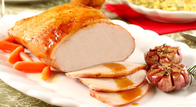 Pernil brasileiro fatiado, servido com molho agridoce e alho assado em um prato branco.