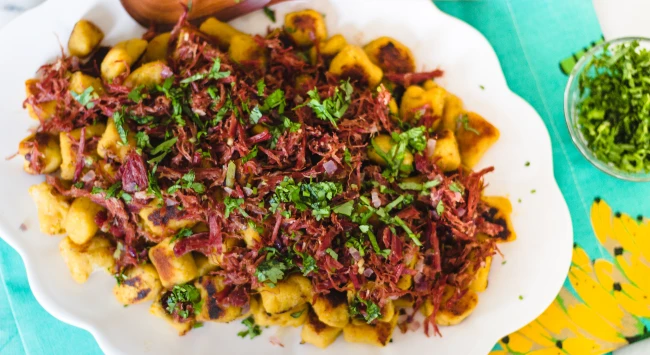 Nhoque com carne seca servido em um prato branco oval.