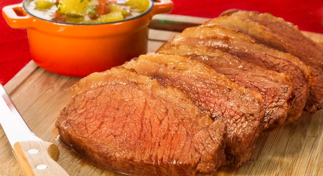 Bifes de picanha grelhados em uma tábua de madeira com uma tigela de vinagrete de laranja ao lado.