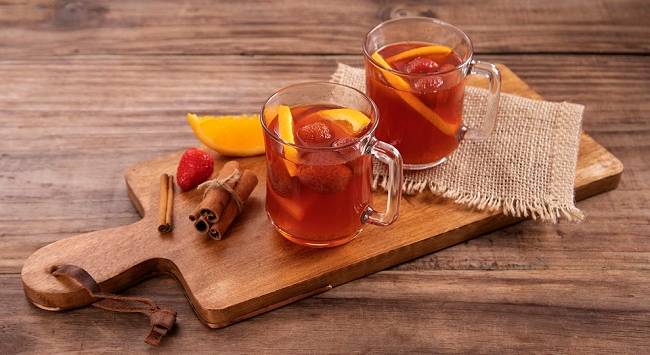 Duas canecas de quentão decorados com morango e laranja, paus de canela, servido sob tábua de madeira