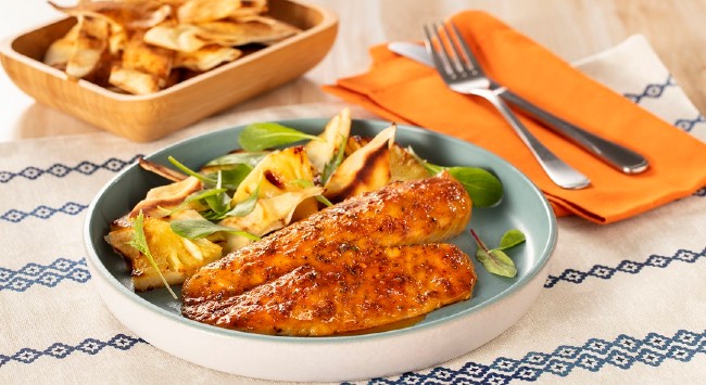 Filés de tilápia grelhados dispostos em um prato azul com salada de abacaxi e croutons.