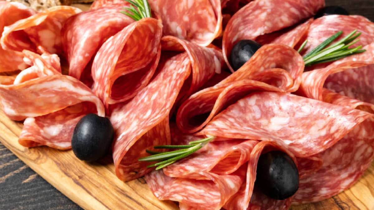 Salame fatiado servido com azeitonas pretas e ramos de alecrim