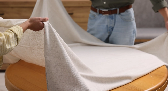 Pessoas esticando uma toalha de mesa branca e simples.