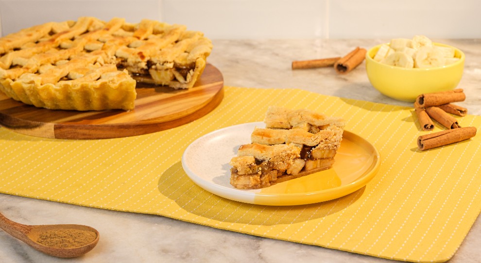 torta de banana trançada em cima de prato amarelo com pedaços de canela ao lado